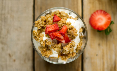 Little glass bowl of homemade granola with greek yoghurt and strawberries, isolated on the wooden rustic table. Flat lay.