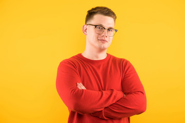 Portrait of young handsome smiling guy with crossed arms on yellow background