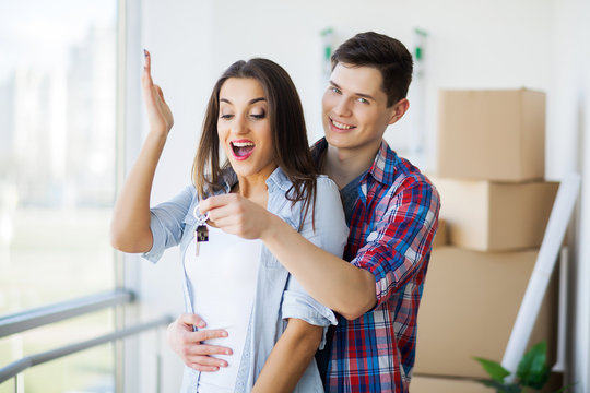 Young Adult Couple Inside Room with Boxes Holding New House Keys Banner.
