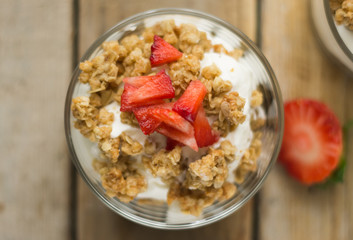Little glass bowl of homemade granola with greek yoghurt and strawberries, isolated on the wooden rustic table. Flat lay.