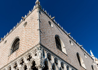 Fototapeta na wymiar Facade of Palazzo Ducale in Piazza San Marco, built in Venetian Gothic style. Architectural detail in Venice, Italy, blue sky in background.