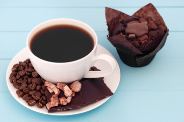 White cup with coffee and chokolate cupkake on a turquoise wooden background.
