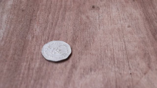 Spin of 5 baht in nonagon shape of ancient Thai money on the wooden floor and stop in reverse of a coin with Garuda form. The concept of finance.