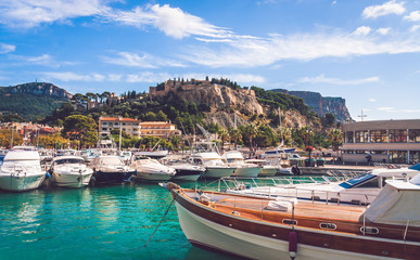 Fototapeta na wymiar Low angle view on Chateau de Cassis castle on top of hill and close up of boats moored in harbour on bright sunny day in Cassis, France