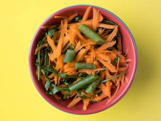 Healthy salad of grated carrots green bean arugula on yellow background