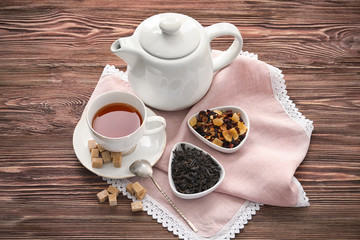 Different types of dry tea leaves and cup of aromatic beverage on wooden table