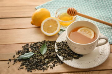 Dry green tea leaves and cup of aromatic beverage with lemon on wooden table