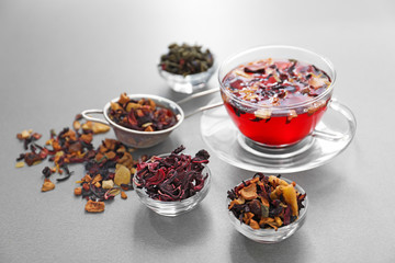 Bowls with different types of dry tea leaves and cup of aromatic beverage on light background