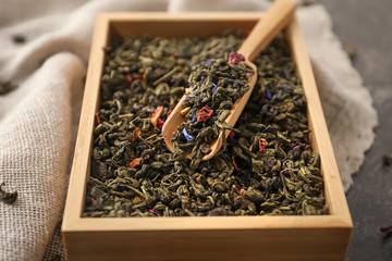 Wooden box and scoop with dry green tea leaves on table