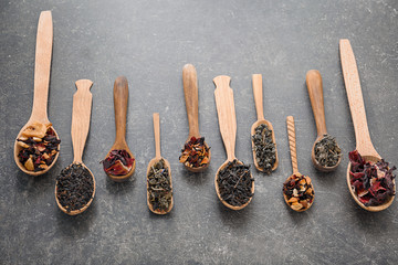 Spoons with different types of dry tea leaves on grey background
