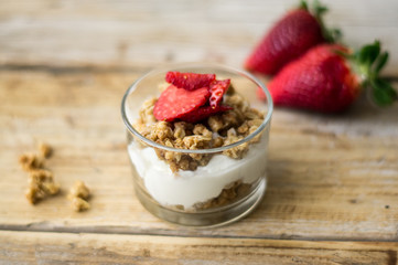Little glass bowl of homemade granola with greek yoghurt and strawberries, isolated on the wooden rustic table