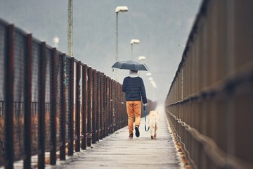 Man with dog is walking in rain