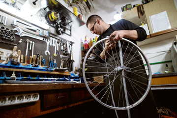 Focused man seeking a correct tool to fix bicycle wheel.