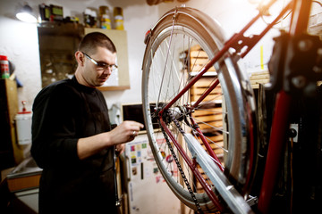 Fototapeta na wymiar Young guy checking bicycle wheel balance in the garage.
