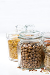 assortment of cereals and legumes in glass jars on white background, vertical