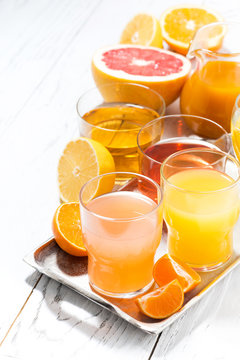 assortment of fresh citrus juices on white table, vertical