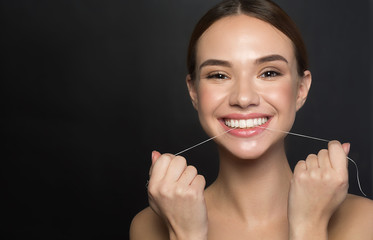 Portrait of positive young woman who is taking care of her teeth. She is holding dental floss and...