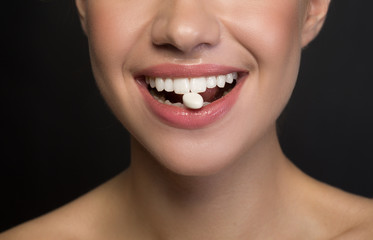 Close up of mouth with white healthy teeth of positive young woman. She is enjoying chewing gum. Isolated on dark background. Fresh breath concept