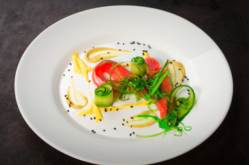 Dish with salmon, seaweed and cucumber. Old black rustic background. Top view