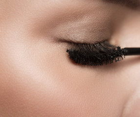 Beauty concept. Close up of closed female eye applying black mascara brush on long eyelashes