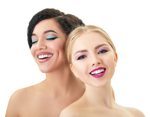 Caucasian blond girl and beautiful young woman posing in studio over white background. Fashion, beauty, glam, youth, makeup. Two beautiful different cheerful female models with perfect smiles.