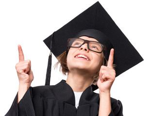Portrait of happy graduate little girl student in black graduation gown, hat and eyeglasses, looking and pointing up with smile - isolated on white background. Educational concept.
