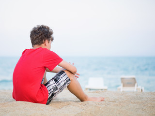 Teen boy on sand on beach - summer vacation, back view. Child looking away. 