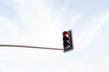 Red traffic light on a horizontal white metal beam, isolated on sky background