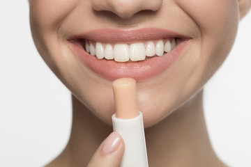 Naklejka premium Beauty concept. Close up half face of cheerful young woman. She is using hygienic balm for lips. Isolated background