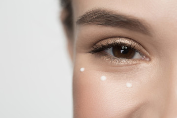 Facial cosmetics concept. Close up of smiley eye of girl. She is looking at camera with joy. Drops of moisturizer cream are around