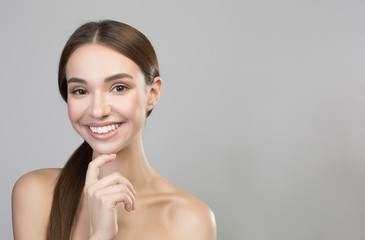 Beauty concept. Portrait of optimistic gorgeous girl is posing naked while looking at camera with smile. She is touching her chin with pleasure. Isolated with copy space in the right side