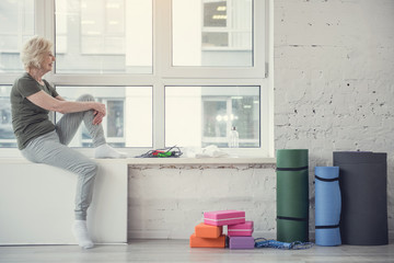 Side view profile of contented aging woman sitting at wide window and smiling. Copy space in right side