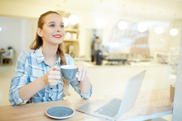 Young woman drinking coffee at the table at coffee shop