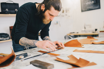 Leather craftsman working making measupenets in patterns at table in workshop studio