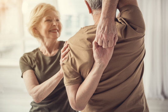 Athletic Retiree Holding His Hands Hooked Behind His Back, Standing With His Back To Camera. Joyful Lady Is In Front Of Him