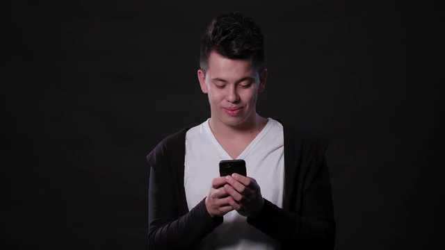 An attractive young man using a phone against a black background. Medium Shot