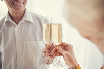 Smiling senior man clinking glasses of wine with aging woman standing in front of him