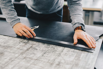 Closeup portrait of unrecognizable leather craftsman working making measupenets in patterns at table in workshop studio