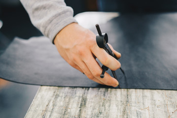 Closeup portrait of unrecognizable leather craftsman working making measupenets in patterns at table in workshop studio