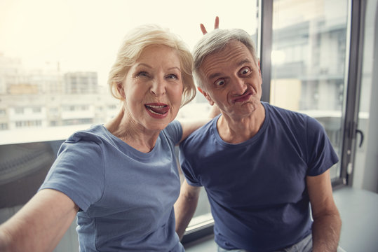 Waist up portrait of funny old man and woman photographing themselves and making faces