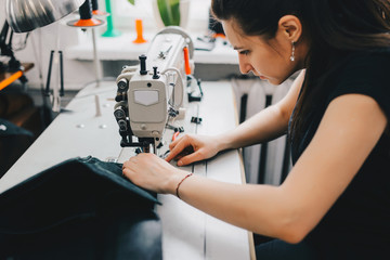 Female artisan threading black leather on sewing machine, close up