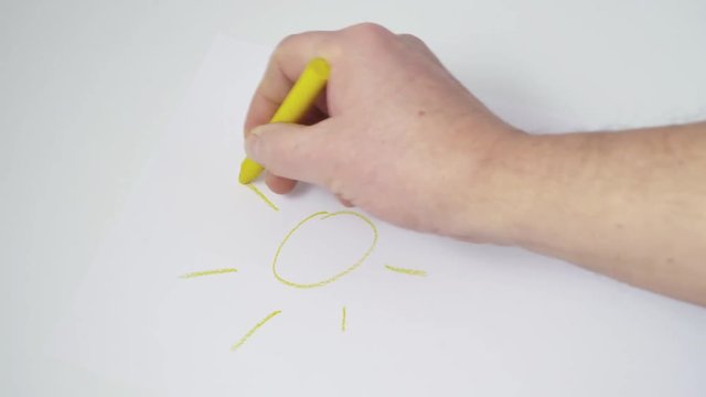 the drawing of a yellow sun made with a wax crayon on a sheet of white paper