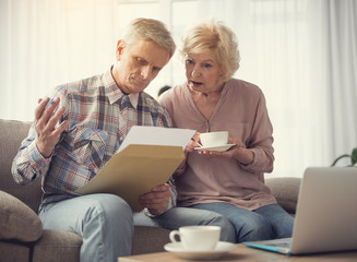 Portrait of calm mature couple concentrated on record in male hand while resting at home with...