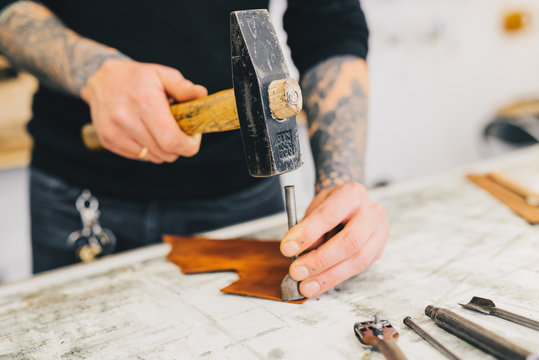 Close up of a leather craftsman working with leather using hammer. Working process in the leather workshop. Man holding crafting tool and working.