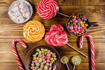 Colorful chocolate candies, lollipops, candy cane and marshmallows on wooden table