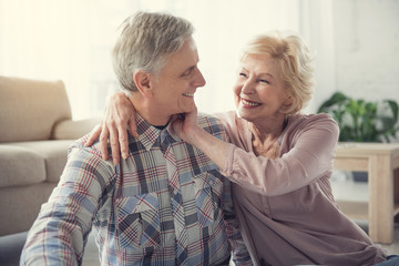 Waist up of glad mature wife and husband spending time together indoors. They are looking at each...