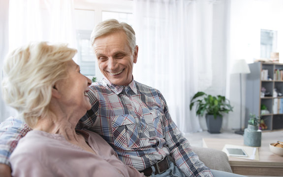 Delighted Senior Man And Woman Hugging On Sofa And Looking Each Other With Fondness. Copy Space In Right Side