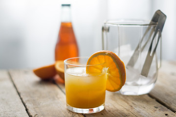 Glass of orange juice / cocktail san pelegrino with ice cubes and a bottle of in the background