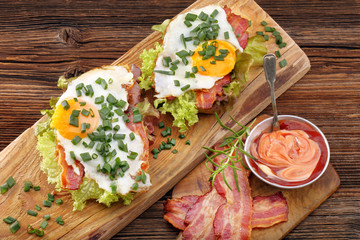Sandwich with fried bacon, egg and vegetables on wooden background