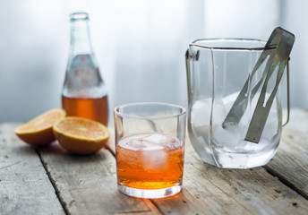 Glass of orange juice / cocktail san pelegrino with ice cubes and a bottle of in the background